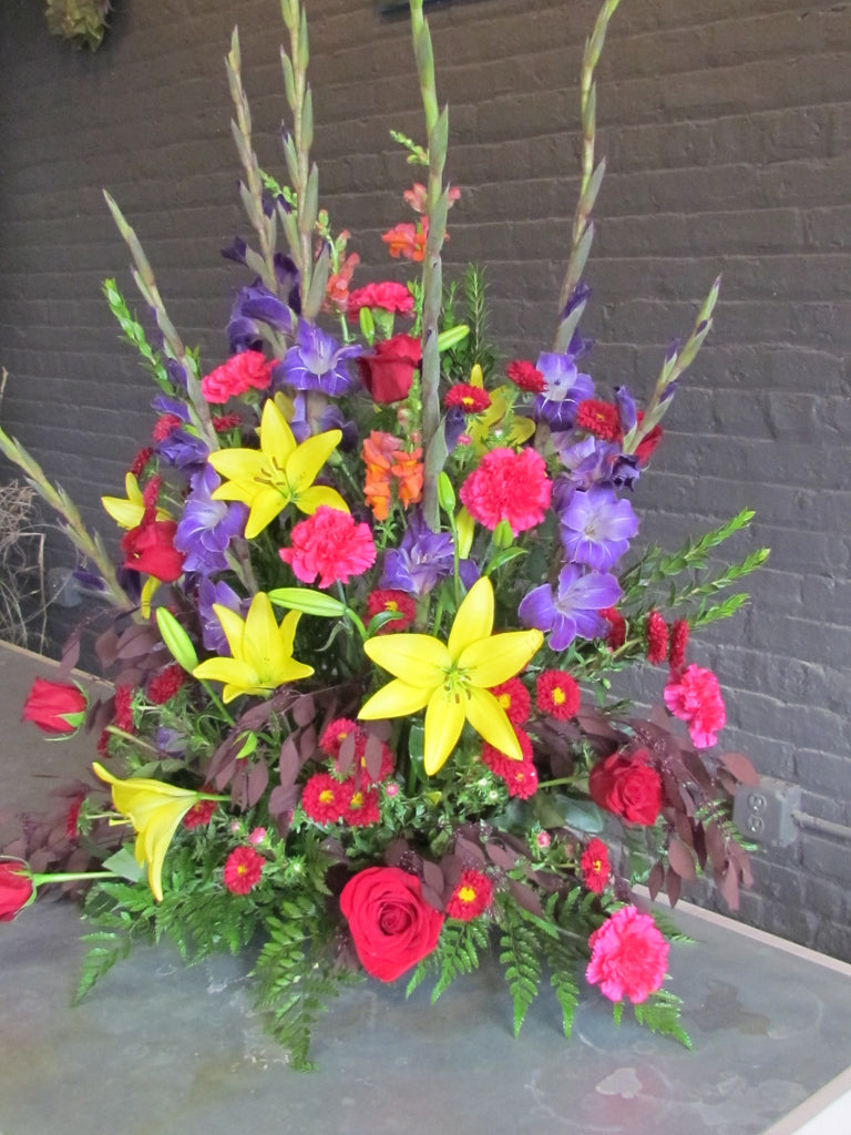 Large multi-colored funeral arrangment with purple, yellow, and red flowers