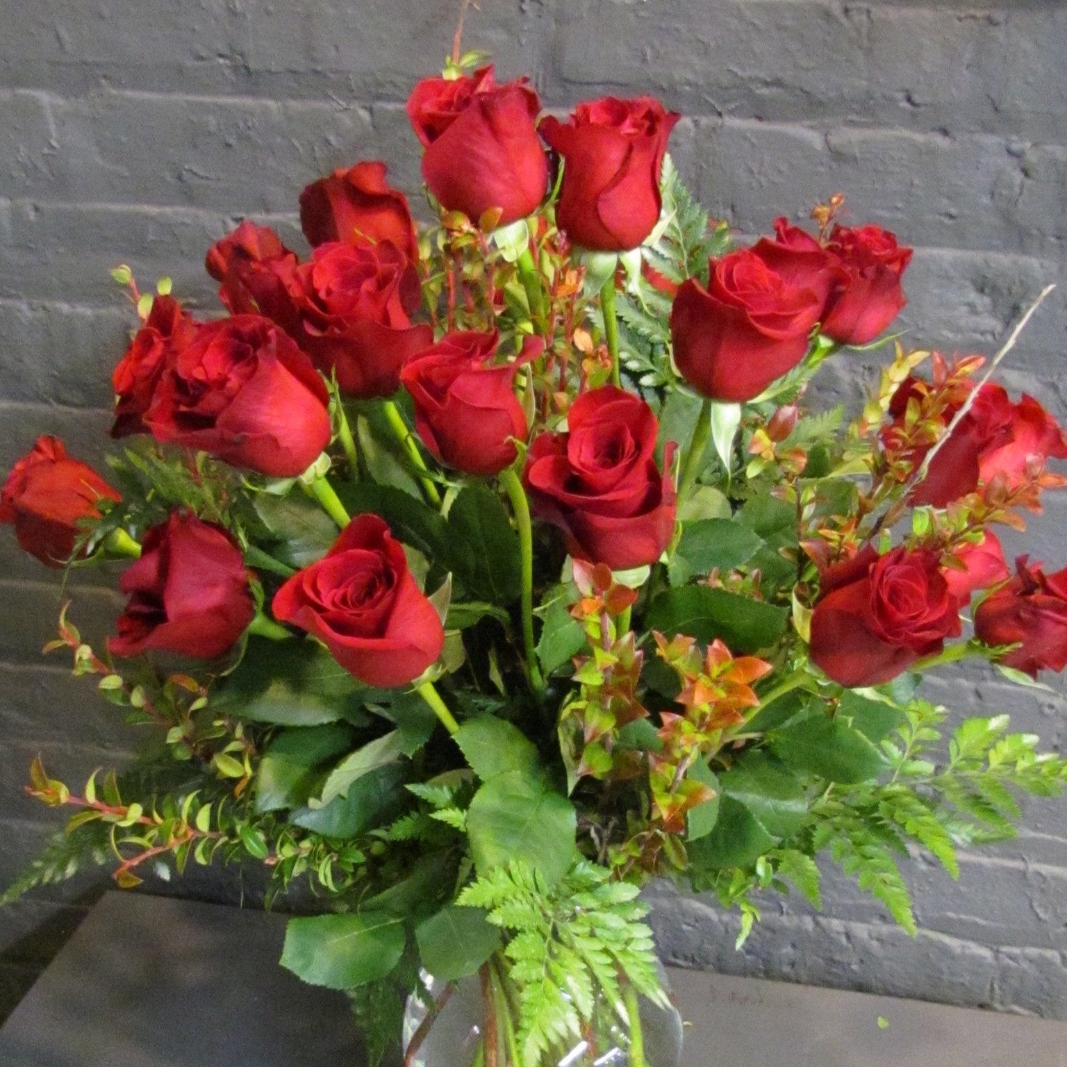 24 roses with greens in a glass vase