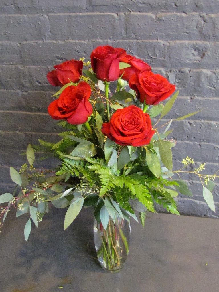 6 red roses with greens in a glass vase